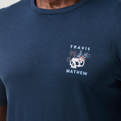 A close up of the chest on the blue TravisMathew shirt, with a skull, and Travis Mathew printed on the chest, with no pocket.