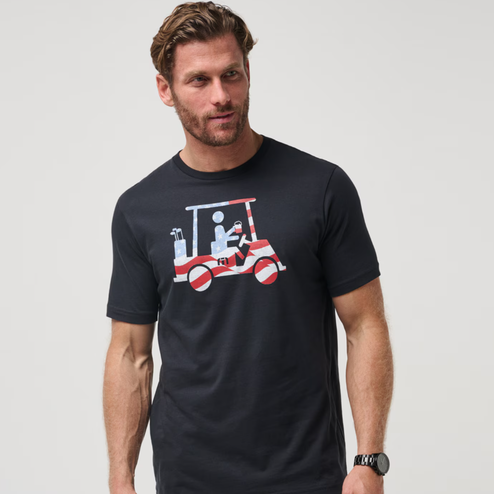 A TravisMathew black t-shirt with a graphic of a stickman riding a golf cart, holding a beverage. The golf cart and stick figure are made from an American Flag.