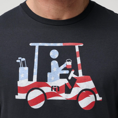 A close up of A TravisMathew black t-shirt with a graphic of a stickman riding a golf cart, holding a beverage. The golf cart and stick figure are made from an American Flag.