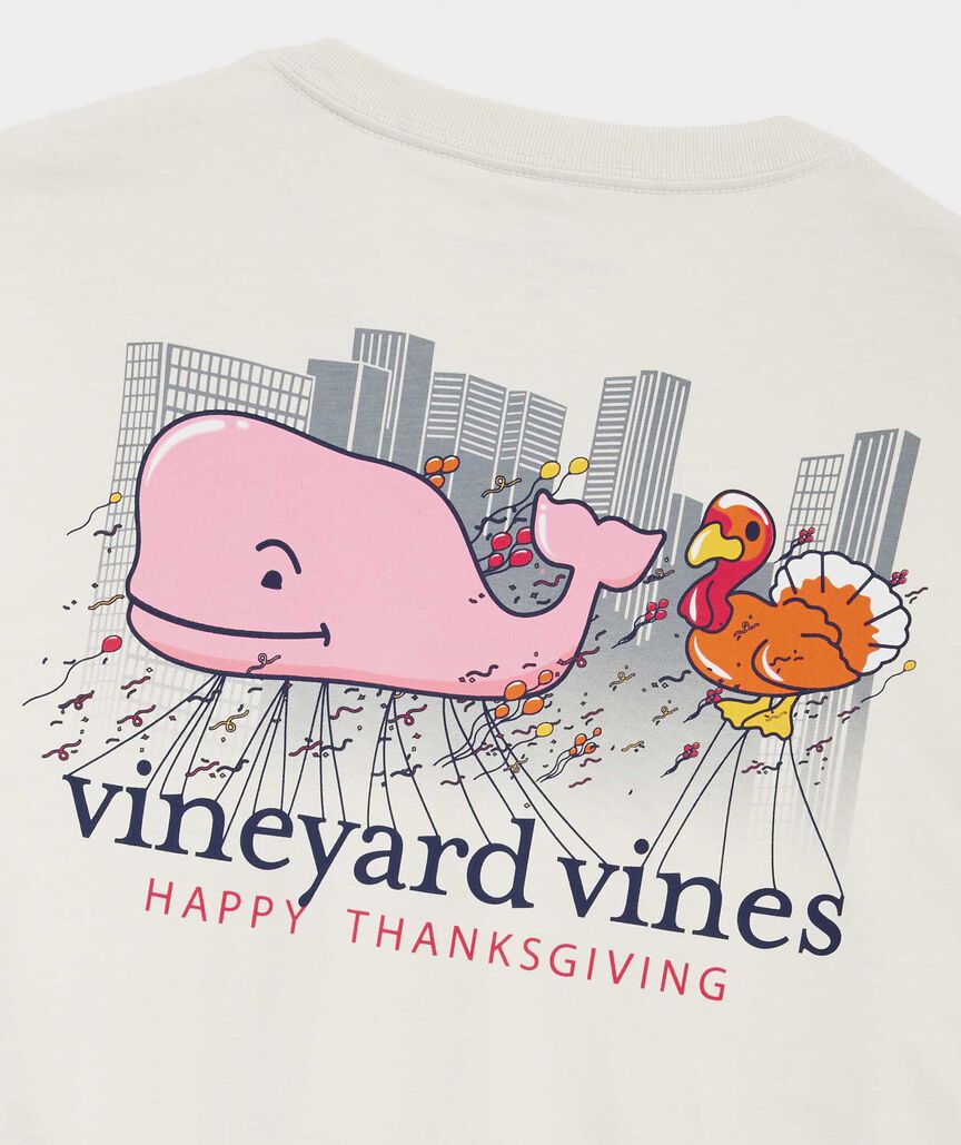 Long sleeve shirt with the Vineyard Vines whale logo next to a Thanksgiving Turkey in the Thanksgiving day parade. The shirt reads, "Vineyard Vines Happy Thanksgiving."