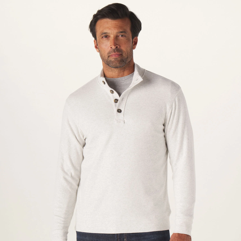 The front of a Puremeso Button Popover shirt from The Normal Brand. The shirt is being worn by a man with black hair, and he is wearing a gray under shirt.The shirt shows 3 buttons at the top, with a popped collar and long sleeves. Shown in the color stone.