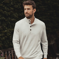 The front of a Puremeso Button Popover shirt from The Normal Brand. The shirt is being worn by a man with black hair, and he is wearing a gray under shirt.The shirt shows 3 buttons at the top, with a popped collar and long sleeves. Shown in the color stone.