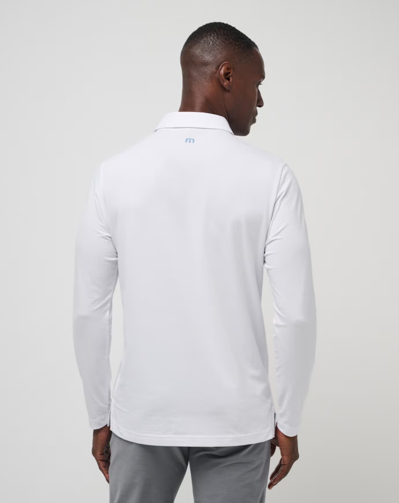 Course Mapper Long Sleeve Polo in all white. Featuring a blue stripe logo across the chest. The polo comes from the brand TravisMathew.