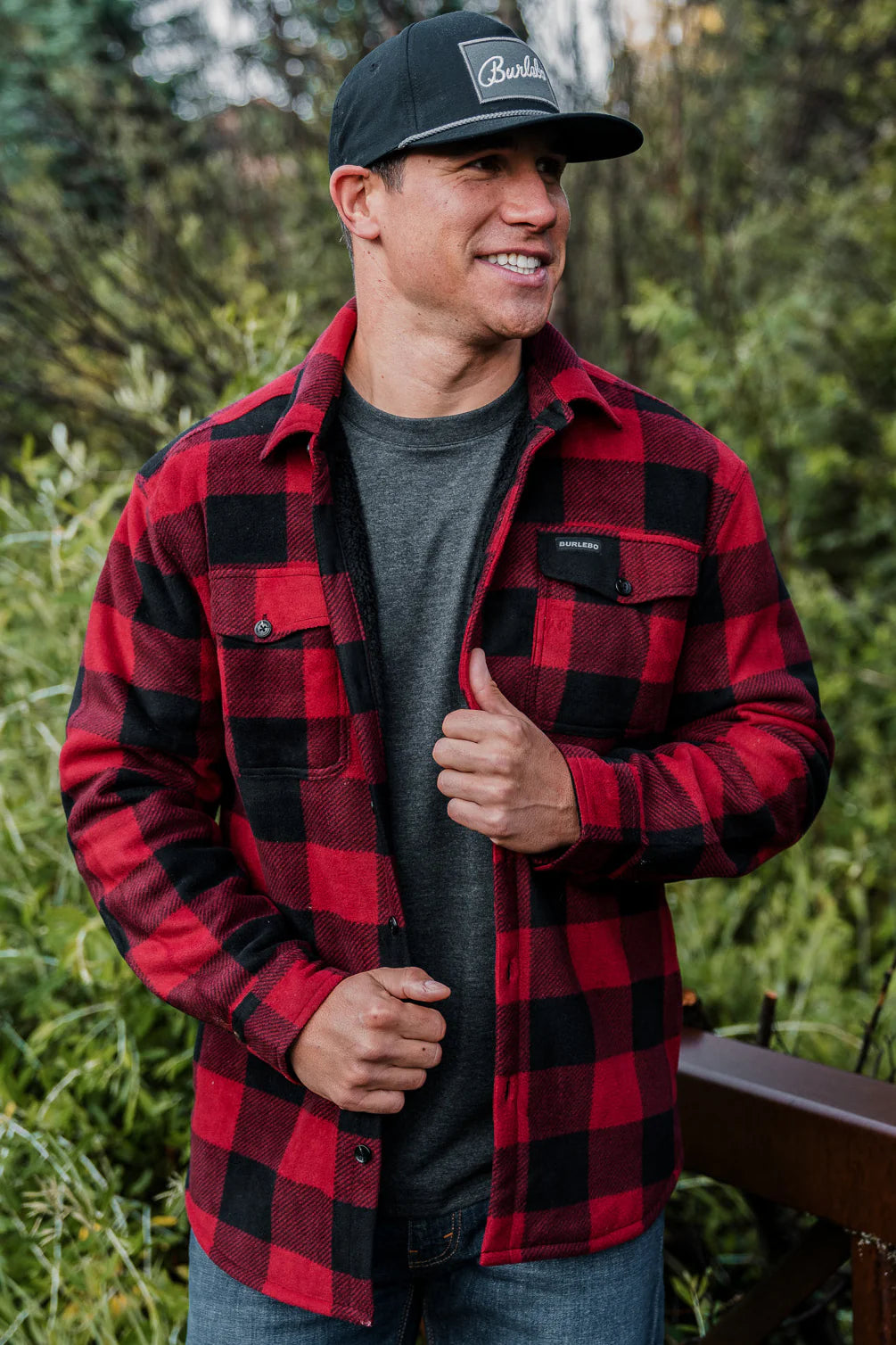 A red plaid shacket being worn by a Burlebo model with a Burlebo hat on. The shacket has two chest pockets and buttons down the front.