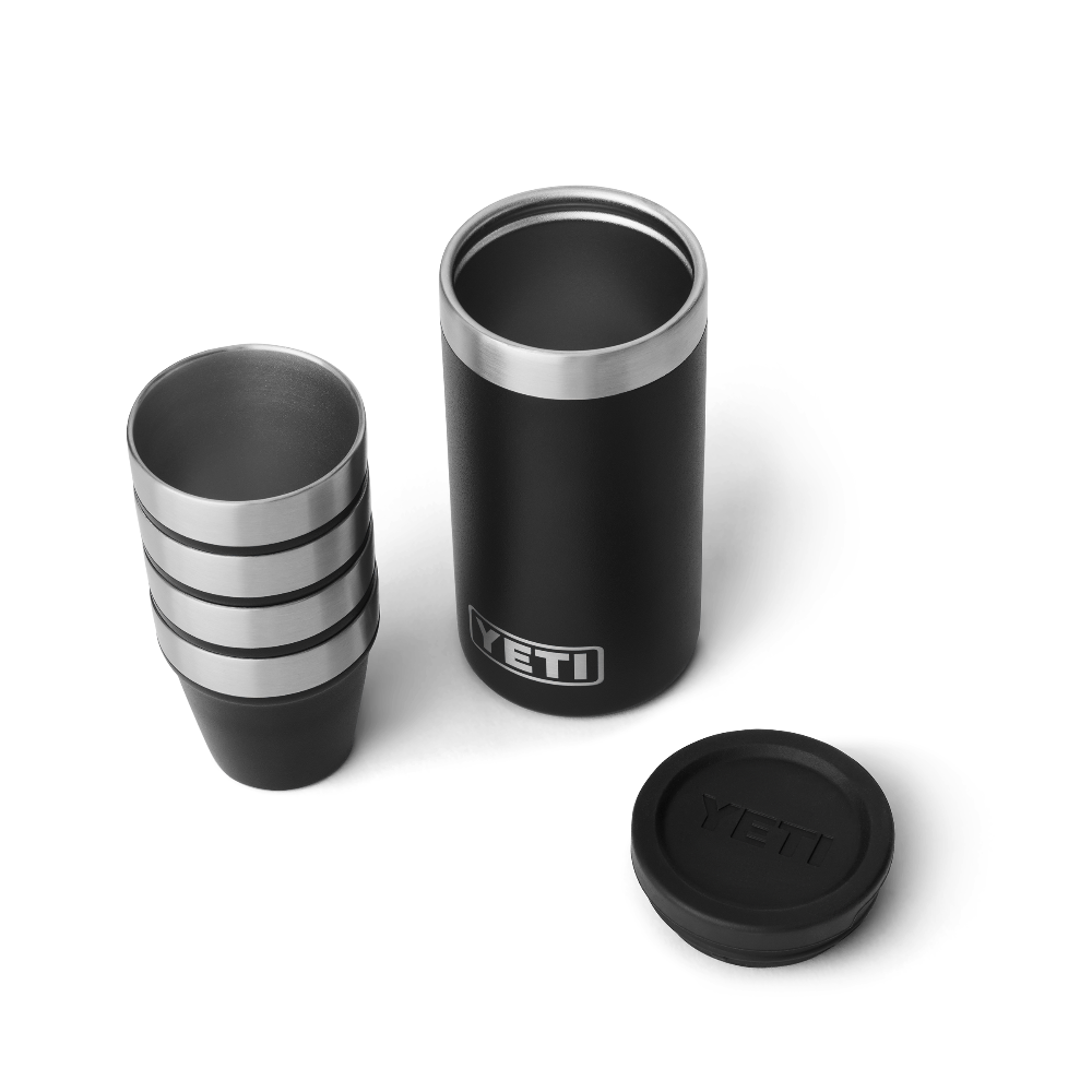 4 black shot glasses stacked on top of one another, sitting next to a black travel case with the lid taken off. The travel case has a silver YETI logo on the front.