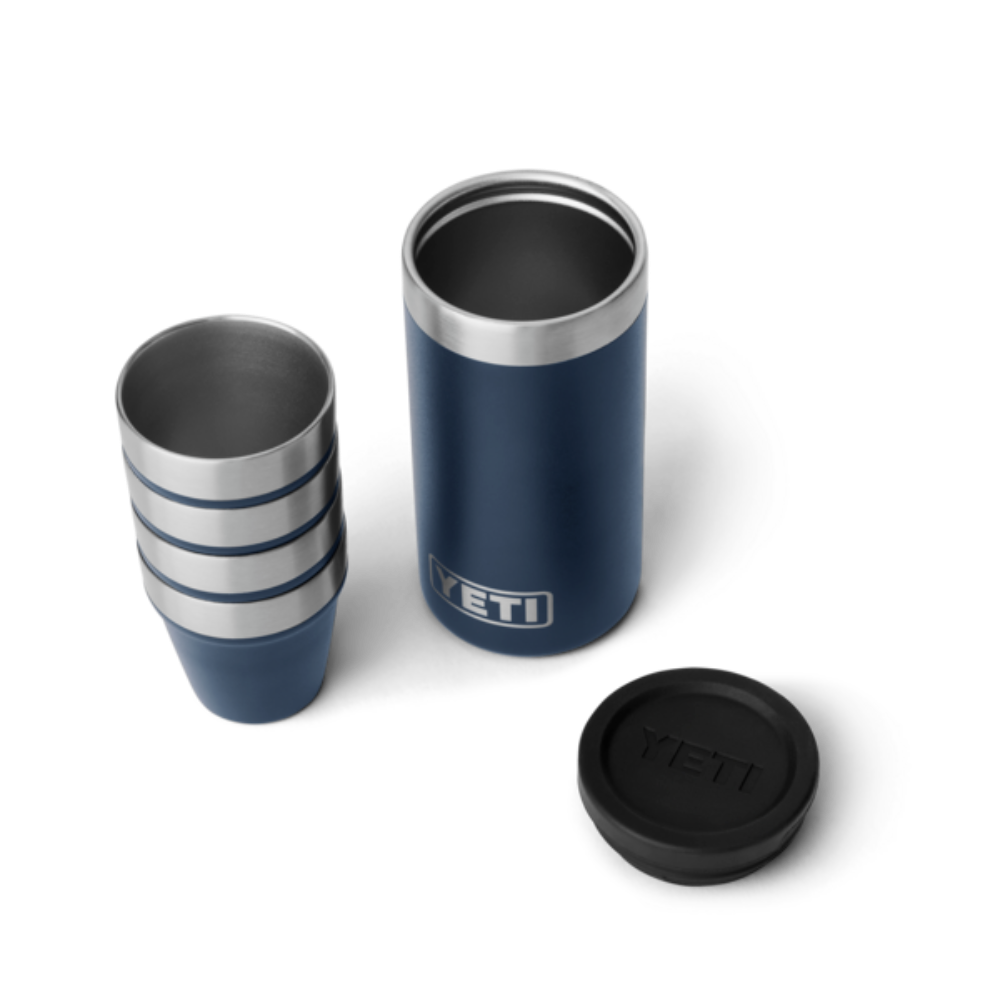 4 navy blue shot glasses stacked on top of one another, sitting next to a navy blue travel case with the lid taken off. The travel case has a silver YETI logo on the front.