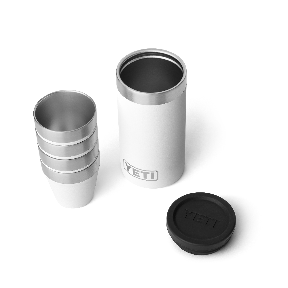 4 white shot glasses stacked on top of one another, sitting next to a white travel case with the lid taken off. The travel case has a silver YETI logo on the front.