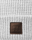 Grey waffle beanie with a brown TravisMathew logo.