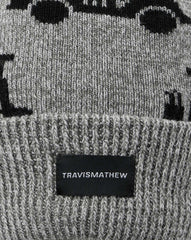 Grey beanie with a palm ball on the top. The beanie has the TravisMathew logo on the front, with the TravisMathew guy drinking in a golf cart logo all around the beanie.